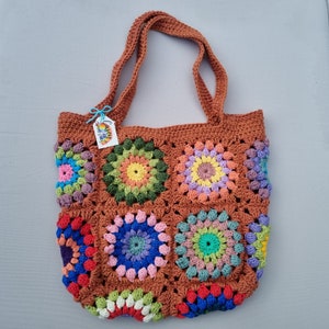 Può includere: Una borsa a mano in crochet marrone con motivi di granny squares colorati. La borsa ha due manici marroni e un'etichetta che dice "Crochet Love".