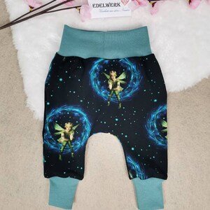 Könnte beinhalten: Schwarze und blaugrüne Babyhose mit einem sich wiederholenden Muster einer Fee in einem blauen und grünen Kreis. Die Hose hat einen breiten elastischen Bund und gekrempelte Beine.