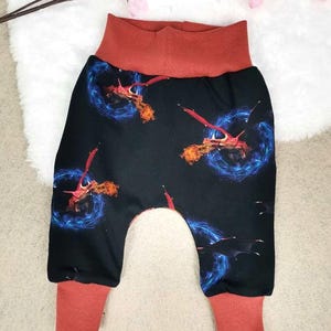 Könnte beinhalten: Schwarze und rote Babyhose mit Drachen-Druck. Die Hose hat einen roten Bund und rote Bündchen. Der Druck zeigt Drachen mit blauen Flammen.