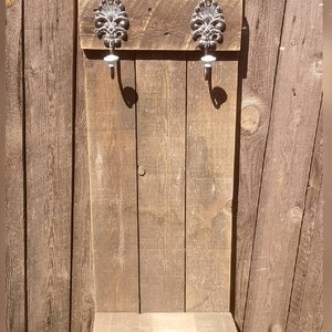 Pode incluir: Cabide de madeira rústico com dois ganchos decorativos e uma prateleira. O cabide é feito de madeira reciclada e tem um acabamento marrom natural.