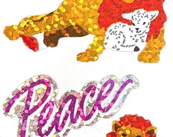 May include: Two stickers featuring a lion with a red mane and a lamb, with the word "Peace" in a sparkly, cursive font above. The lion and lamb are in shades of gold, brown, and white.