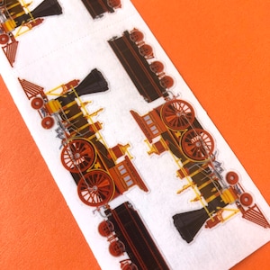 May include: A sheet of stickers featuring illustrations of vintage steam locomotives in shades of brown, black, and yellow. The trains are depicted with large red wheels, prominent smokestacks, and detailed mechanical components on a white background.
