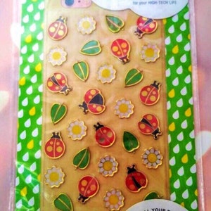May include: A package of dimensional stickers featuring ladybugs, daisies, and leaves. The stickers are red, yellow, green, and white. The package reads "puffies" and "Style all your devices!"