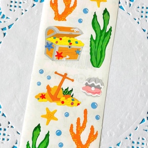 May include: A sheet of colorful ocean-themed stickers. Designs include an open treasure chest filled with gold, anchors, starfish, coral, seaweed, bubbles, and clams. The stickers are on a white background.
