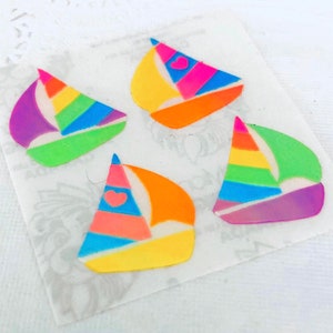 May include: Four colorful sailboat stickers. Each sticker features a vibrant rainbow sail with a different color scheme, including pink, orange, yellow, green, and purple. Some sails have a heart detail. The stickers are on a white background.