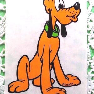 May include: Orange cartoon dog with black ears and a black nose, wearing a green collar. The dog is sitting with its legs extended. The image has the text "©DISNEY" at the bottom.