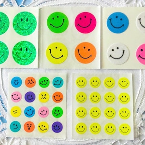 May include: Sheets of colorful smiley face stickers in various sizes and colors, including green, yellow, orange, pink, blue, and white. Some stickers have glittery surfaces. The stickers are arranged on white backing sheets.