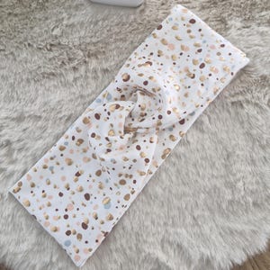 Könnte beinhalten: Weißer geknöpfter Stirnband mit einem Konfetti-Muster in Gold, Braun und Rosa.