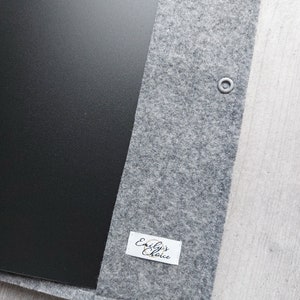 以下が含まれることがあります： 黒い内側と「Emily's Choice」と書かれた白いラベルが付いた灰色のフェルト製ラップトップスリーブです。