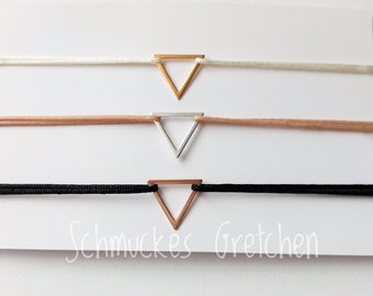 May include: Three bracelets featuring a central triangle charm on a thin cord. The top bracelet has a gold triangle on a white cord, the middle has a silver triangle on a tan cord, and the bottom has a rose gold triangle on a black cord. Text reads Schmuckes Gretchen.
