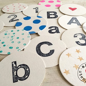Puede incluir: Un juego de 14 posavasos redondos y blancos con varios diseños. Los diseños incluyen lunares, estrellas, corazones y letras. Los posavasos están hechos de un material grueso y absorbente y son perfectos para proteger las superficies de derrames y arañazos.