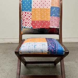 May include: Wooden folding chair with a patchwork fabric seat and backrest. The fabric features a variety of patterns and colors, including polka dots, floral prints, and solid blocks of color. The chair has a dark brown wooden frame.