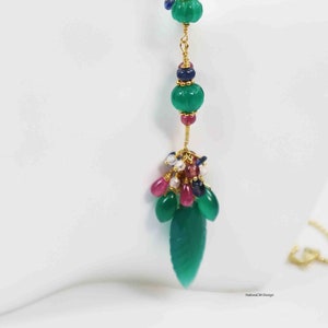 Puede incluir: Un collar de cadena de oro con un colgante de piedra preciosa verde. El colgante presenta un grupo de piedras preciosas más pequeñas en rosa, azul y blanco, y una piedra preciosa verde más grande con forma de hoja.