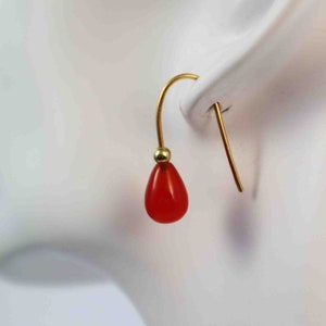 Puede incluir: Pendientes de aro dorados con una piedra preciosa roja en forma de lágrima.