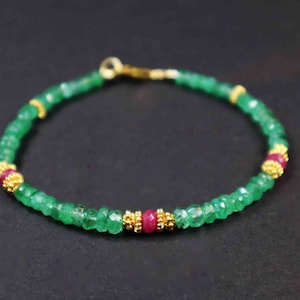 Puede incluir: Un brazalete de piedras preciosas de esmeralda verde y rubí con detalles dorados. El brazalete está hecho de pequeñas cuentas facetadas y tiene un diseño simple y elegante.