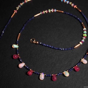 May include: A delicate necklace with a double strand of blue sapphire beads and gold accents. The necklace features alternating teardrop-shaped opal and ruby gemstones.