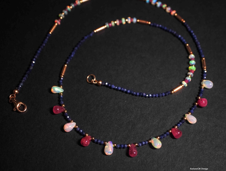 May include: A delicate necklace with a double strand of blue sapphire beads and gold accents. The necklace features alternating teardrop-shaped opal and ruby gemstones.