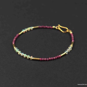 Könnte beinhalten: Ein zartes goldenes Armband mit einem Verschluss. Das Armband besteht aus kleinen, runden Perlen in Weiß-, Rosa- und Goldtönen.