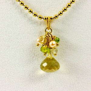 May include: A gold chain necklace with a pendant featuring a cluster of green and pink gemstones and a large, faceted, yellow gemstone.