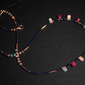 May include: A delicate necklace with a double strand of dark blue beads and a single strand of alternating opal and ruby beads. The necklace features a lobster clasp closure.