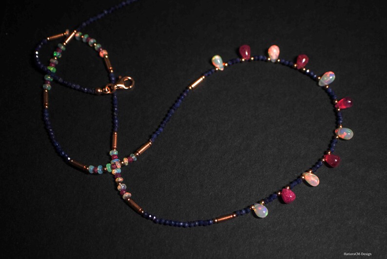 May include: A delicate necklace with a double strand of dark blue beads and a single strand of alternating opal and ruby beads. The necklace features a lobster clasp closure.
