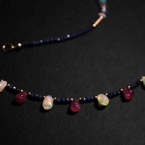 May include: A delicate necklace with a gold chain and blue beads. The necklace features alternating teardrop-shaped opal and ruby gemstones.