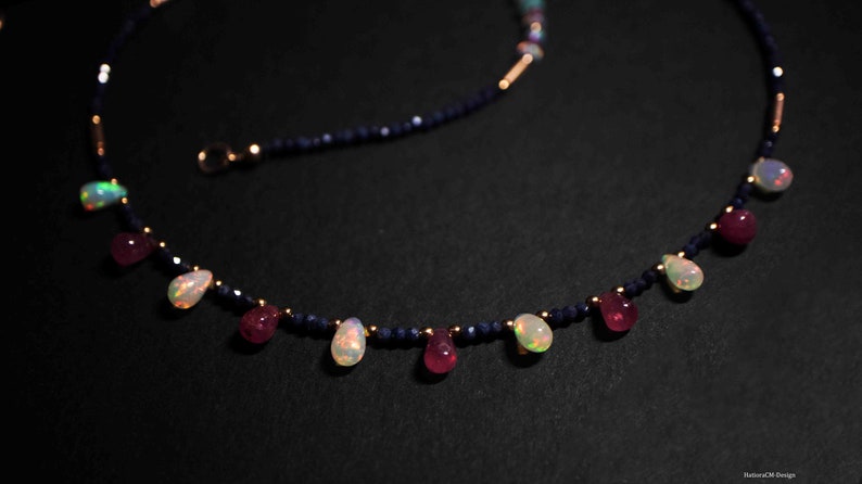 May include: A delicate necklace with a gold chain and blue beads. The necklace features alternating teardrop-shaped opal and ruby gemstones.