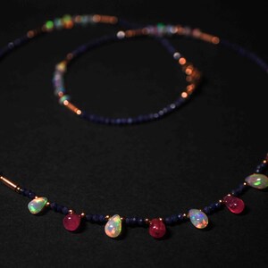 May include: A necklace made of blue and copper beads with teardrop-shaped opal and ruby gemstones.