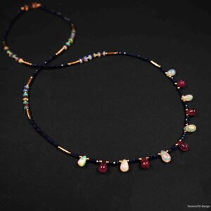 May include: A delicate necklace with a dark blue beaded chain and dangling teardrop-shaped opal and ruby gemstones. The necklace features gold accents and is a beautiful statement piece.