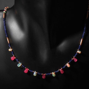 May include: A delicate necklace with alternating pink and white teardrop-shaped gemstones, separated by small blue beads and gold spacers.