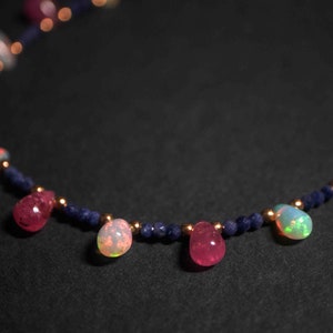 May include: A delicate necklace with a gold chain and alternating blue, pink, and white gemstone beads. The necklace features a repeating pattern of small blue beads and larger, teardrop-shaped gemstones.