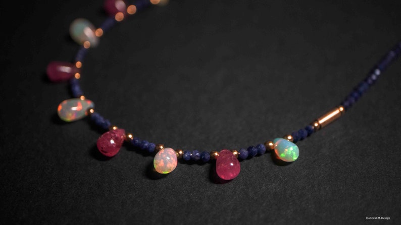 May include: A delicate necklace with a gold chain and alternating blue, pink, and white gemstone beads. The necklace features a repeating pattern of small blue beads and larger, teardrop-shaped gemstones.