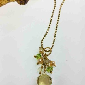 May include: A gold chain necklace with a pendant featuring a large, light brown gemstone surrounded by smaller green and pink gemstones.