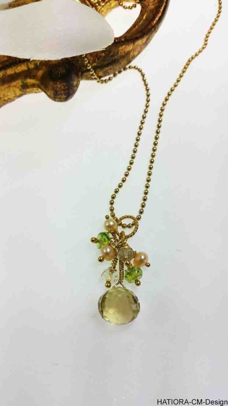 May include: A gold chain necklace with a pendant featuring a large, light brown gemstone surrounded by smaller green and pink gemstones.