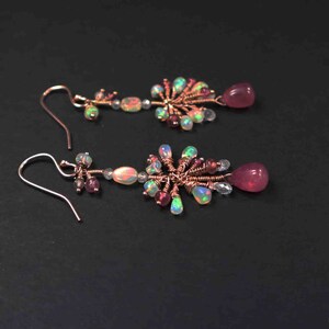 Peut inclure: Une paire de boucles d'oreilles pendantes avec un design en fil de cuivre. Les boucles d'oreilles pr&eacute;sentent des pierres pr&eacute;cieuses roses et iris&eacute;es.