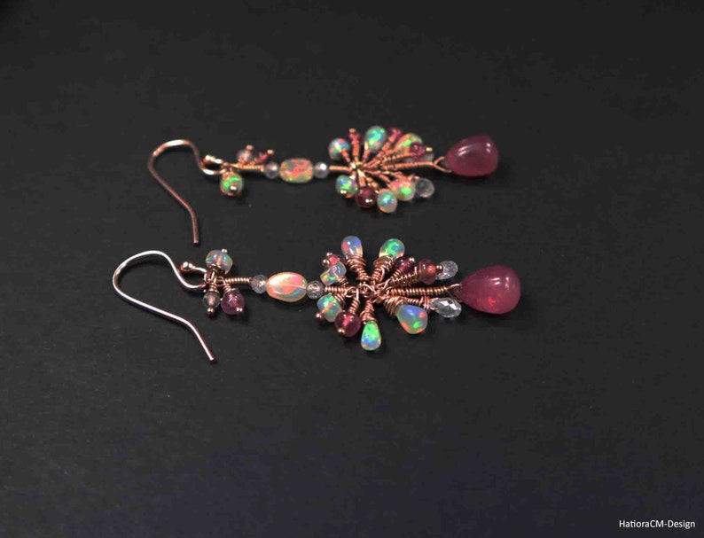 Peut inclure: Une paire de boucles d'oreilles pendantes avec un design en fil de cuivre. Les boucles d'oreilles pr&eacute;sentent des pierres pr&eacute;cieuses roses et iris&eacute;es.