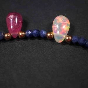 May include: A close-up of a necklace with alternating pink and white teardrop-shaped stones, separated by small blue beads.