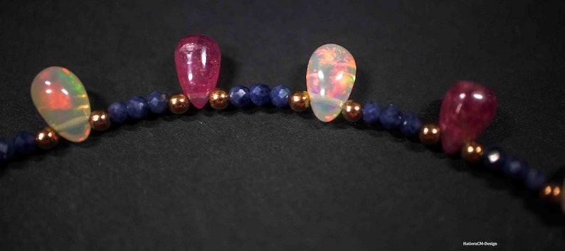 May include: A close-up of a necklace with alternating pink and white teardrop-shaped stones, separated by small blue beads.