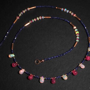 May include: A delicate necklace with a mix of blue sapphire, pink ruby, and white opal beads. The necklace features a teardrop design with alternating gemstone colors.