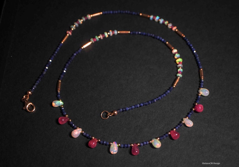 May include: A delicate necklace with a mix of blue sapphire, pink ruby, and white opal beads. The necklace features a teardrop design with alternating gemstone colors.