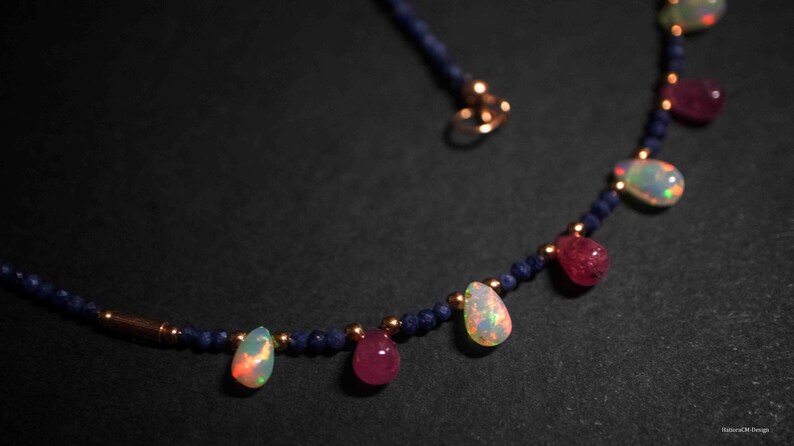 May include: A delicate necklace with a blue beaded chain and teardrop-shaped gemstones. The gemstones are a mix of pink and iridescent white.