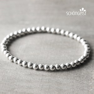 Könnte beinhalten: Ein silbernes Armband mit einem schlichten Design. Das Armband besteht aus kleinen, runden Perlen, die auf einer dünnen Schnur aufgefädelt sind.