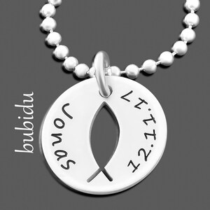 Op de afbeelding: Een zilverkleurige hangerketting met een kogelketting. De hanger is een cirkelvormige schijf met een uitgesneden vissymbool. De naam "Jonas" en de datum "12.11.17" zijn op de hanger gegraveerd. Het woord "bubidu" staat aan de zijkant gedrukt.
