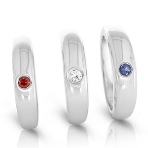 May include: Three silver rings with a single gemstone set in each. The rings are arranged from left to right with a red gemstone, a clear gemstone, and a blue gemstone.