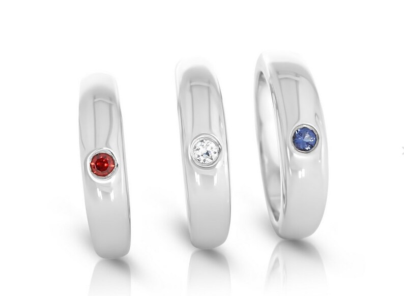 May include: Three silver rings with a single gemstone set in each. The rings are arranged from left to right with a red gemstone, a clear gemstone, and a blue gemstone.