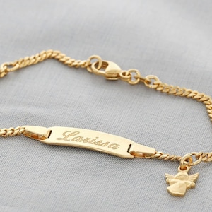 Könnte beinhalten: Goldkette Armband mit einem Namensschild Anhänger mit dem Namen "Larissa" und einem Engel Anhänger.