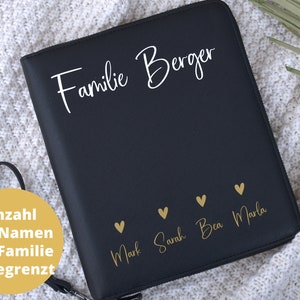 Könnte beinhalten: Schwarzer Leder-Familienordner mit goldener Beschriftung. Der Text lautet "Familie Berger" und enthält die Namen "Mark, Sarah, Bea und Marla" mit einem goldenen Herzen neben jedem Namen. Der Text "Anzahl der Namen der Familie unbegrenzt" befindet sich auf einem gelben Etikett.