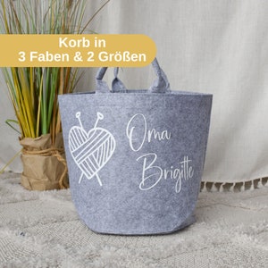 Könnte beinhalten: Grauer Filz-Aufbewahrungskorb mit weißen Henkeln und einem weißen Design eines Herzens mit Garn und Stricknadeln. Der Text "Oma Brigitte" ist auf den Korb gedruckt.
