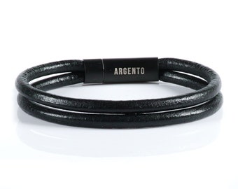 May include: A black leather bracelet with two bands. The bracelet has a magnetic clasp with the word "ARGENTO" engraved on it. The bracelet is shown on a white background.