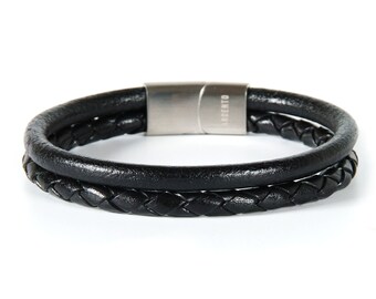 Puede incluir: Pulsera de cuero negro con diseño trenzado y cierre magnético plateado. El cierre tiene la palabra "Argento" grabada.